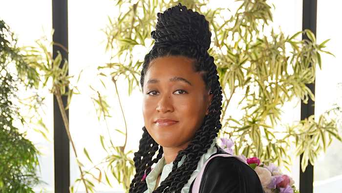 Naomi Osaka wears her hair in a bun on top of her head and smiles at the camera.